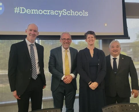 group of people standing in front of projection screen with text reading #DemocracySchools